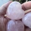 A person holding three heart shaped rose quartz stones.