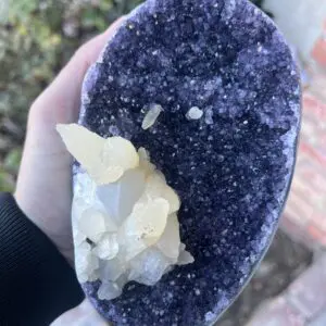 A person is holding a Uruguayan Amethyst Cut Base with Secondary Calcite 1,048 grams in their hand.