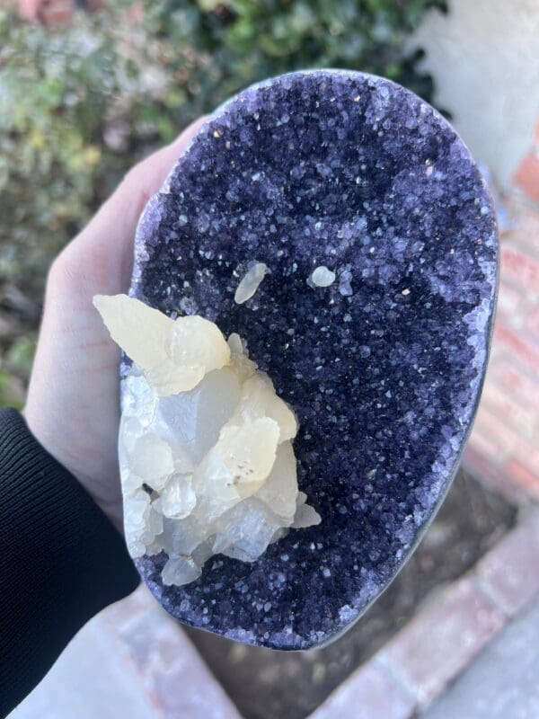 A person is holding a Uruguayan Amethyst Cut Base with Secondary Calcite 1,048 grams in their hand.