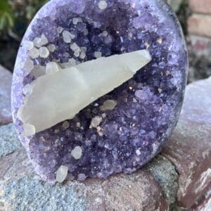 A piece of Uruguayan Amethyst Cut Base with Secondary Calcite 1,212 grams sitting on top of a rock.