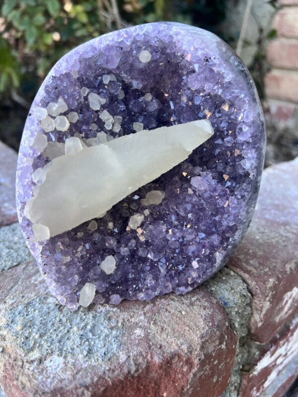 A piece of Uruguayan Amethyst Cut Base with Secondary Calcite 1,212 grams sitting on top of a rock.