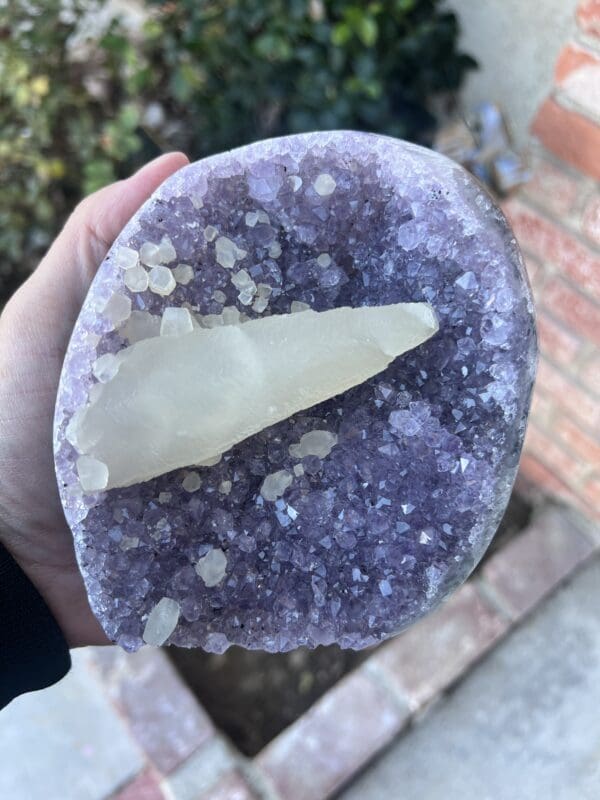 A person holding a piece of Uruguayan Amethyst Cut Base with Secondary Calcite 1,212 grams in their hand.