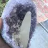 A person holding a Uruguayan Amethyst Cut Base with Secondary Calcite 1,212 grams crystal in their hand.
