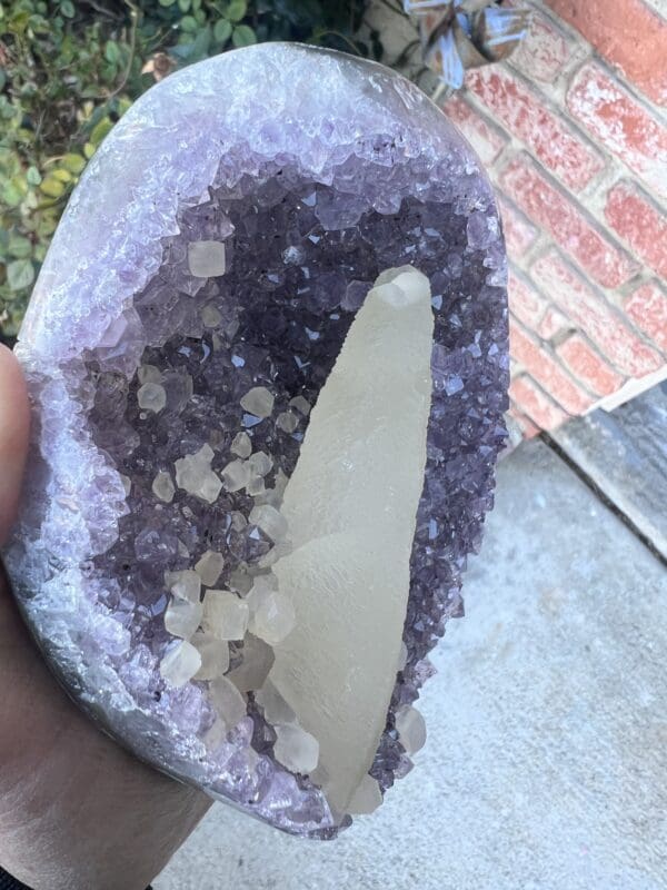 A person holding a Uruguayan Amethyst Cut Base with Secondary Calcite 1,212 grams crystal in their hand.