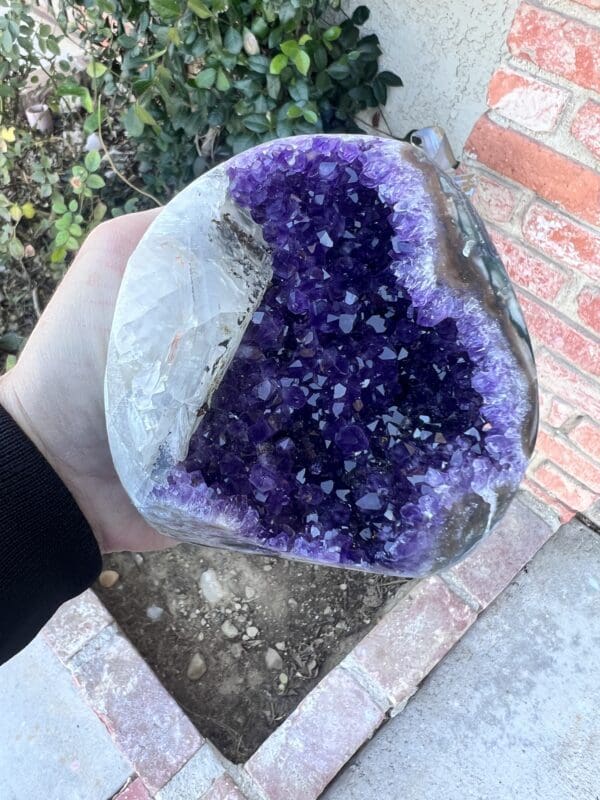 A Uruguayan Amethyst Cut Base with Secondary Calcite 932 grams stone in a person's hand.