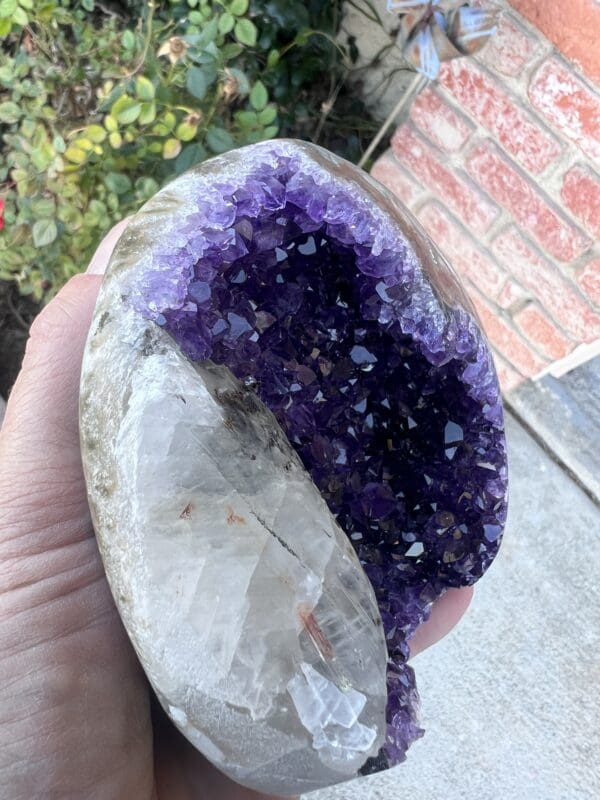 An Uruguayan Amethyst Cut Base with Secondary Calcite 932 grams in a person's hand.