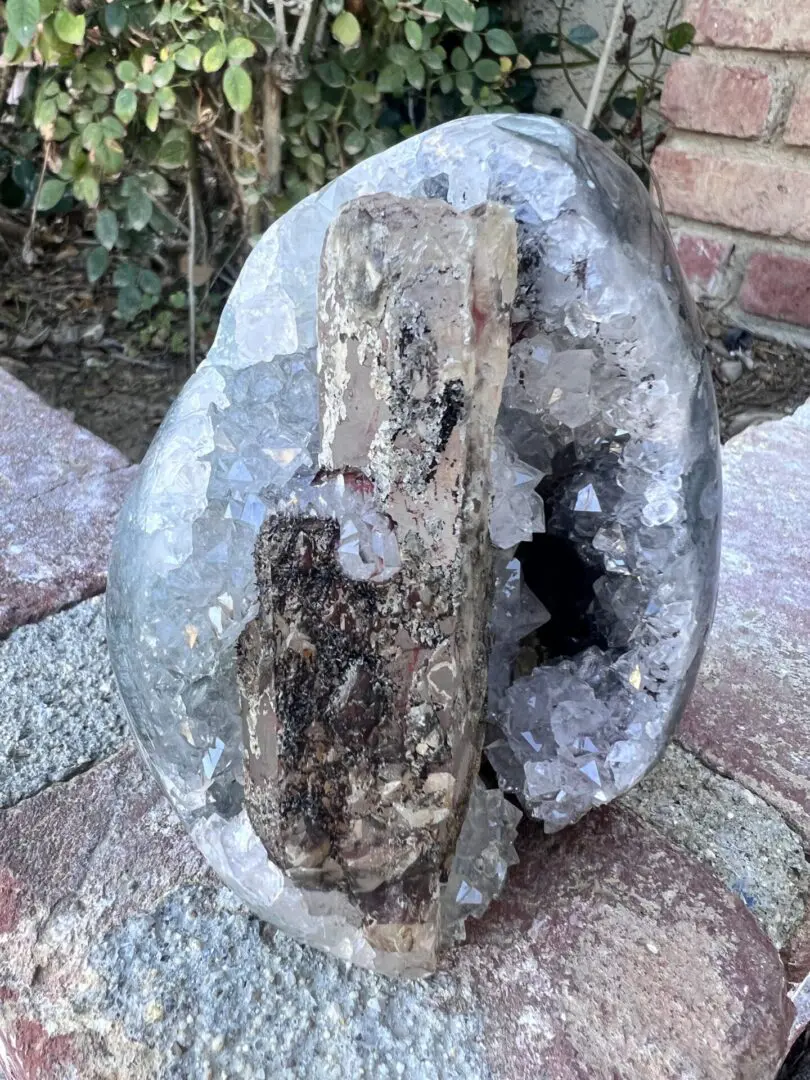 A rock with a piece of Uruguayan Clear Quartz Cut Base Geode with Secondary Calcite sitting on top of it.