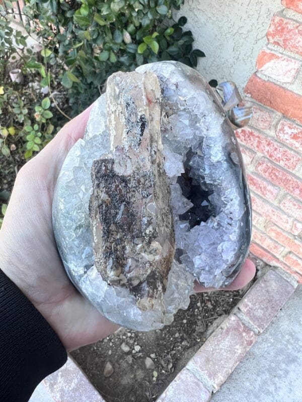 A person holding a piece of Uruguayan Clear Quartz Cut Base Geode with Secondary Calcite in their hand.