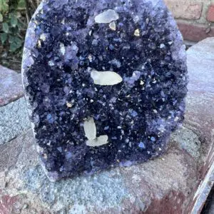 An Uruguayan Amethyst Cut Base with Secondary Calcite 822 grams sitting on top of a brick wall.