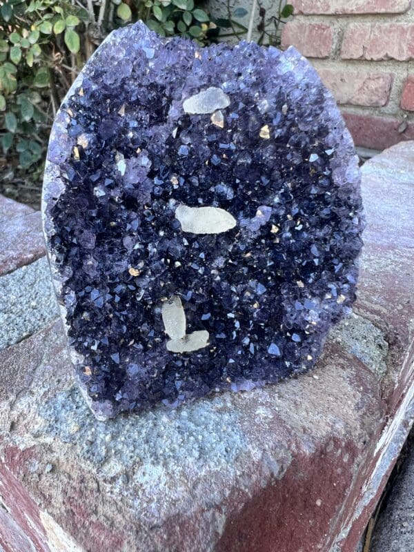 An Uruguayan Amethyst Cut Base with Secondary Calcite 822 grams sitting on top of a brick wall.