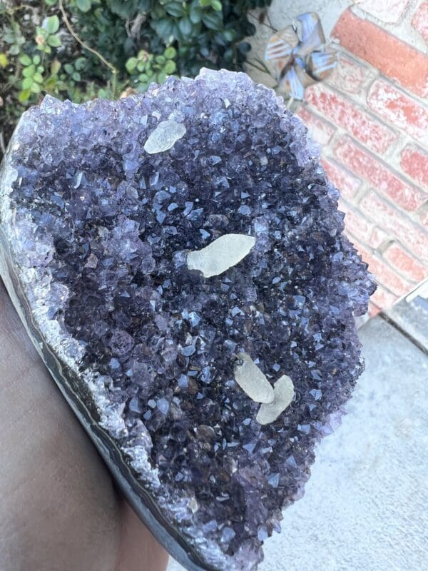 A Uruguayan Amethyst Cut Base with Secondary Calcite 822 grams in a person's hand.