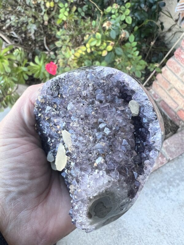 A person holding a Uruguayan Amethyst Cut Base with Secondary Calcite 822 grams rock in their hand.