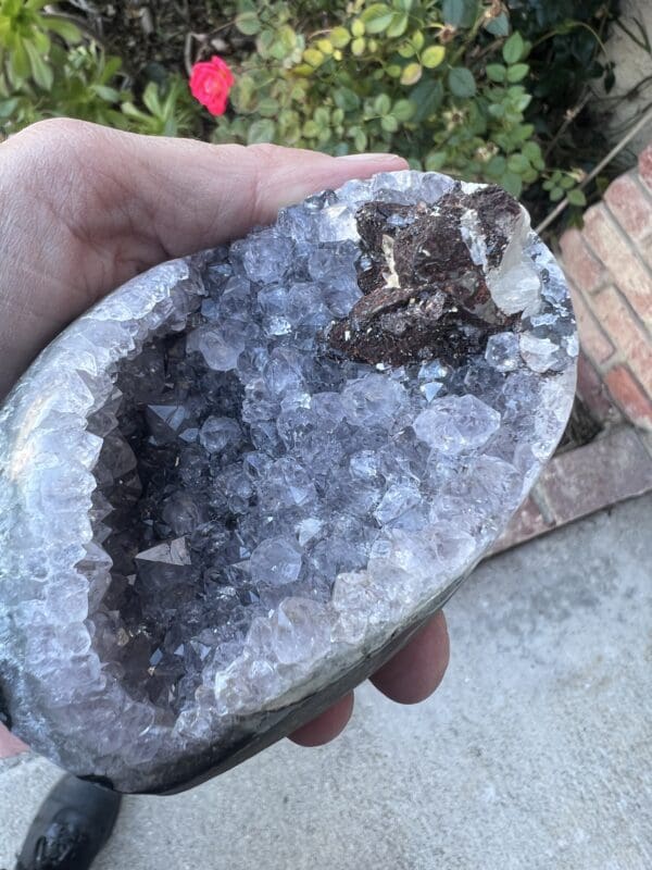 A person holding a piece of Uruguayan Amethyst Cut Base with Secondary Calcite 412 grams in their hand.