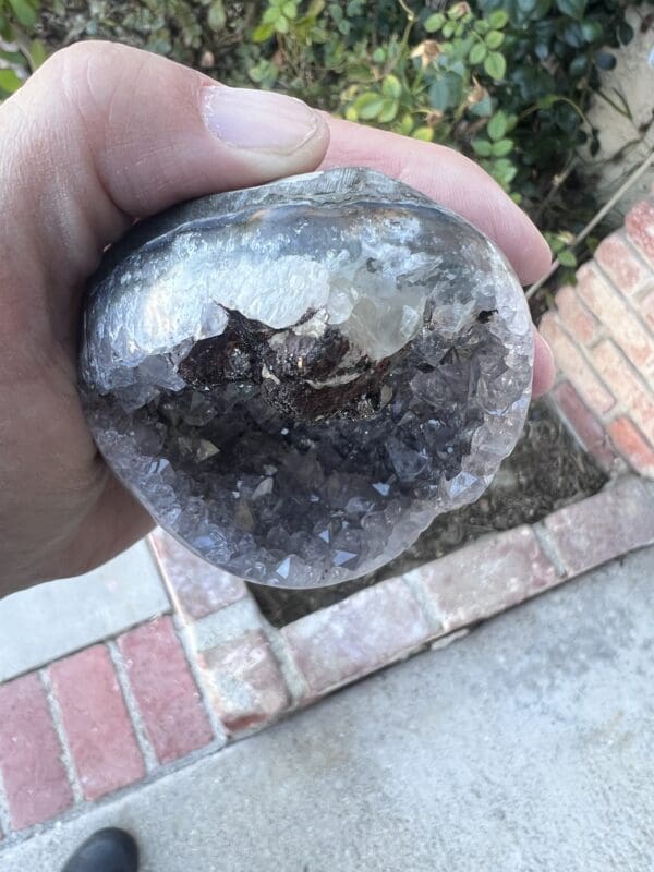 A person holding a Uruguayan Amethyst Cut Base with Secondary Calcite 412 grams in their hand.