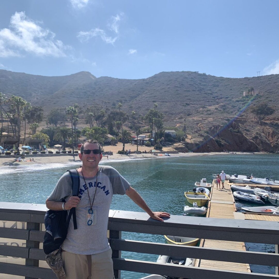 A man standing on the side of a pier near some boats.